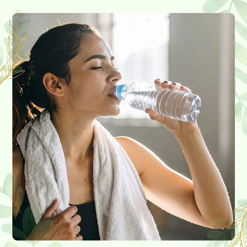 Woman drinking water after a workout with a towel around her neck.
