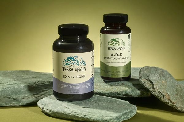 Two bottles of Terra Origin supplements on stone surfaces with a green background