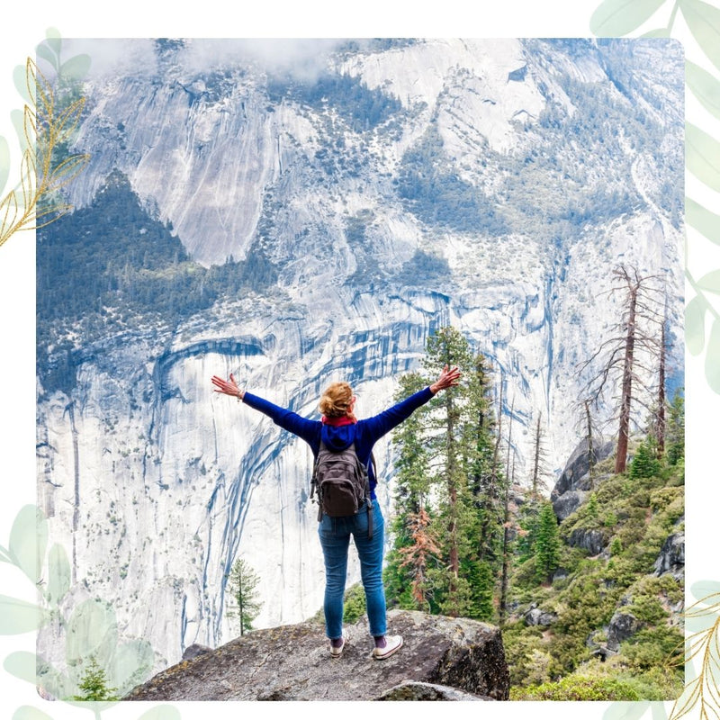 Person standing on a rock with arms outstretched in front of a mountainous landscape