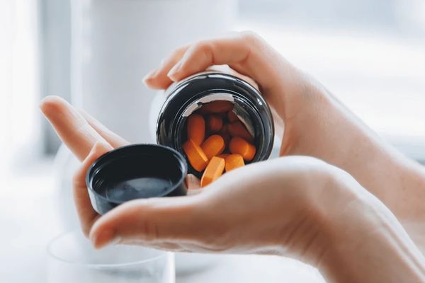 Close-up of hands pouring bright orange supplement capsules