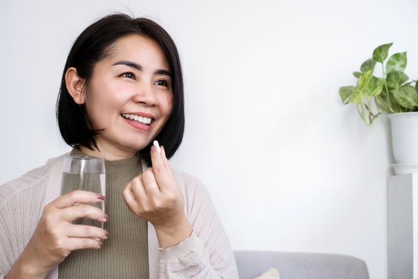 Smiling woman holding a glass of water taking a supplement capsule