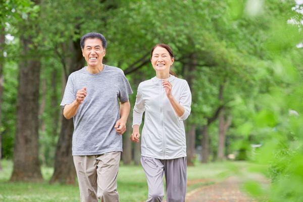 Older man and woman jogging together along a tree-lined path